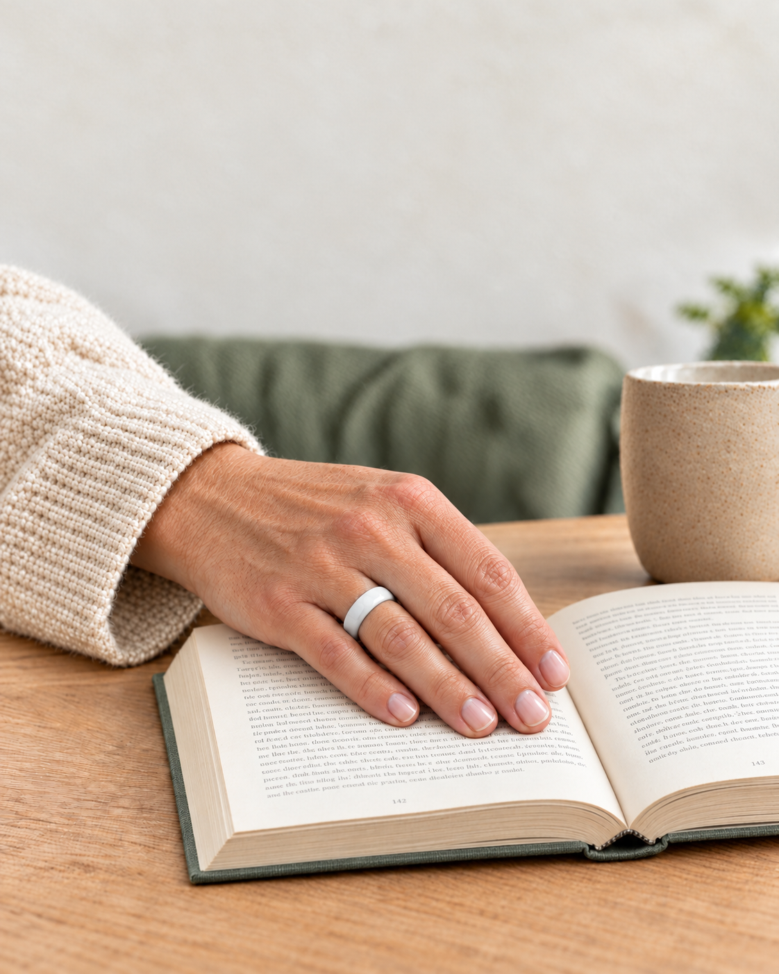 Eine Hand mit weißem Keramikring ruht auf einem offenen Buch. KI-inszenierte Alltagsszene.